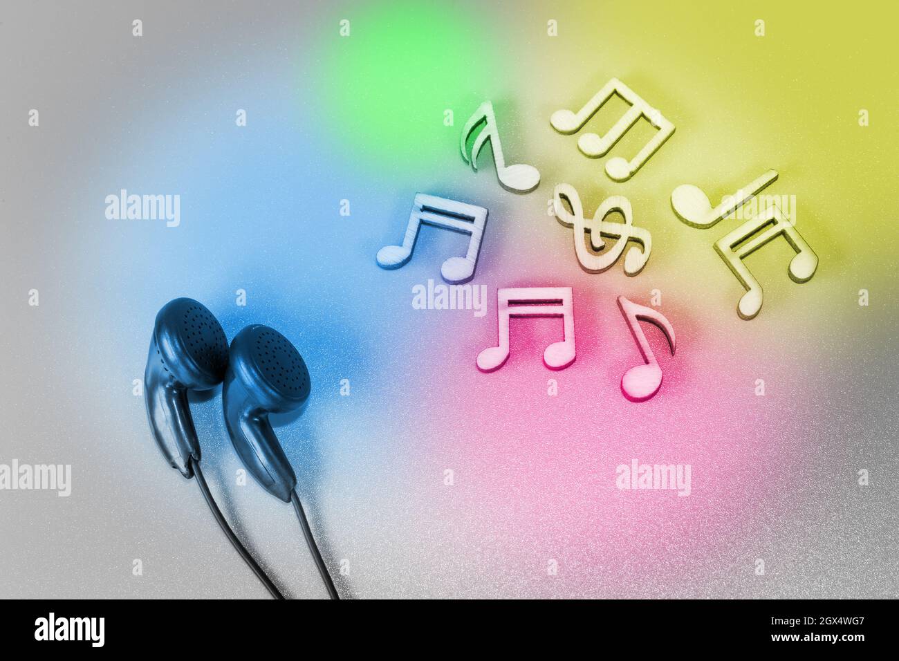 Cuffie e note musicali in legno su sfondo bianco illuminate da macchie colorate Foto Stock