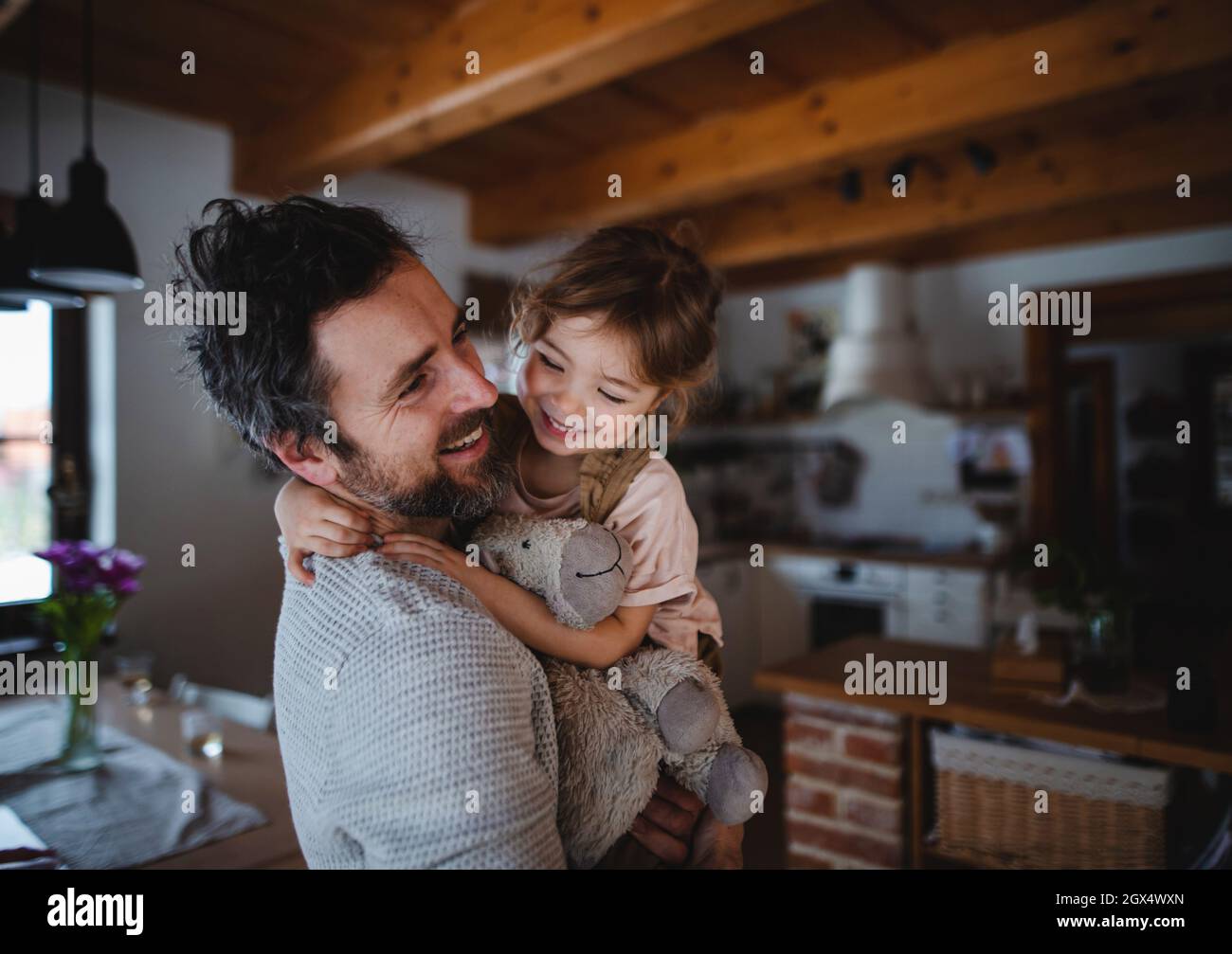 Padre maturo con una piccola figlia in piedi in casa, tenendo e abbracciando. Foto Stock