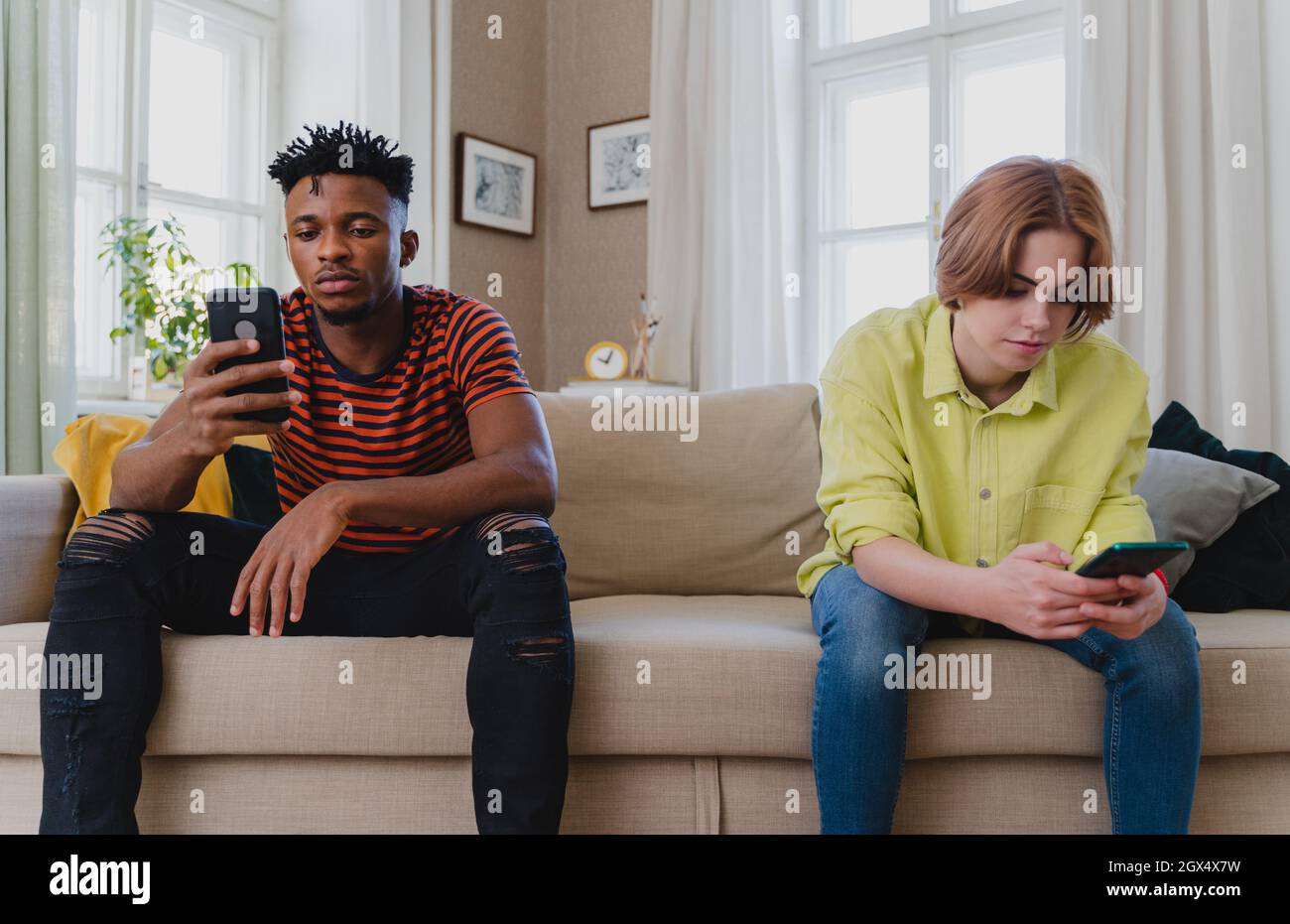 Giovane coppia biraciale addicted a smartphone seduti sul divano a casa, social media concetto. Foto Stock