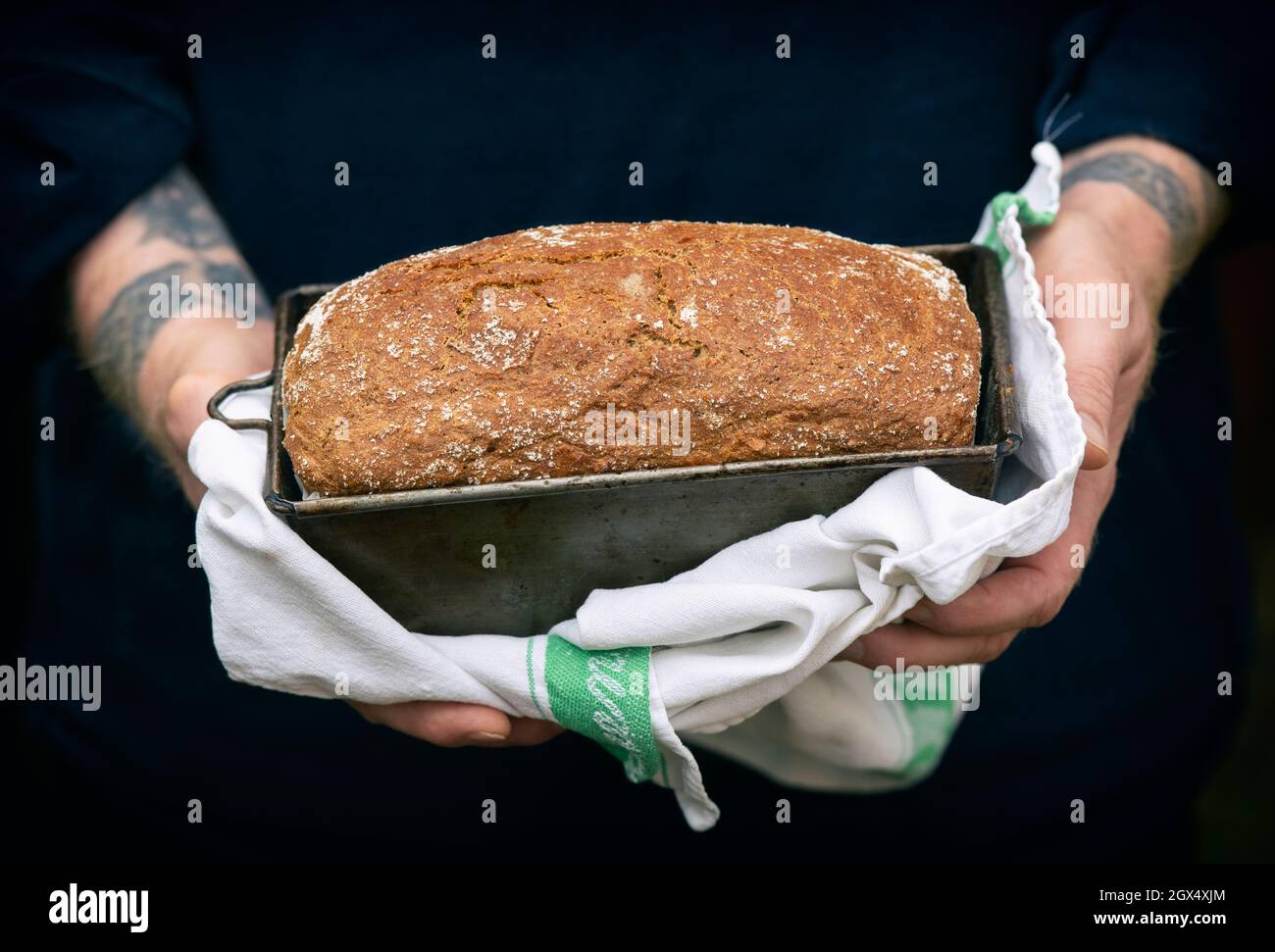 Uomo che tiene una pagnotta fatta in casa di farro di pane integrale di soda appena sfornato in una scatola Foto Stock