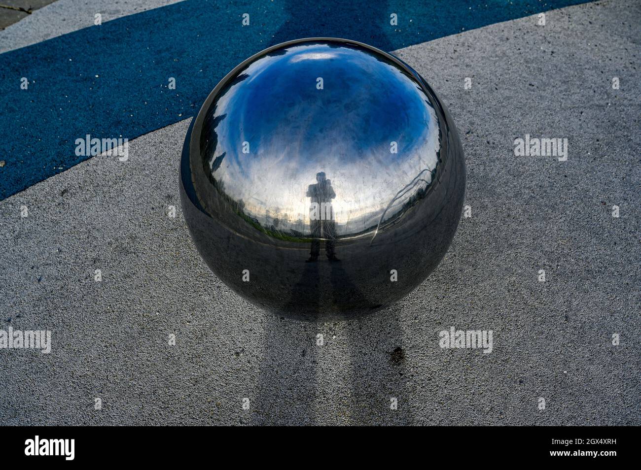 fotografo che si specchia in grande sfera di metallo lucido Foto Stock