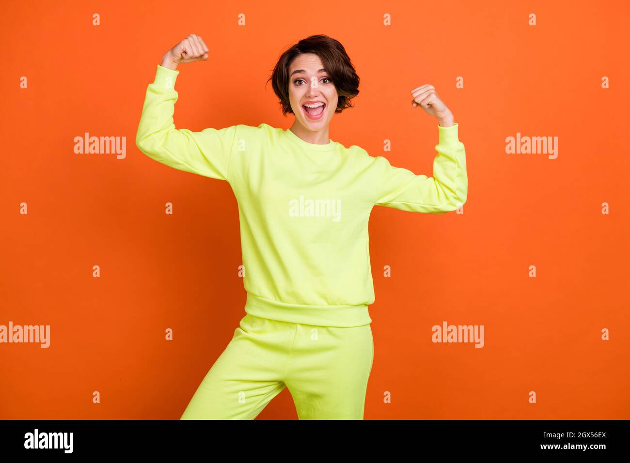 Foto di felice allegro giovane forte donna mostra mani muscoli buon umore isolato su sfondo di colore arancione Foto Stock