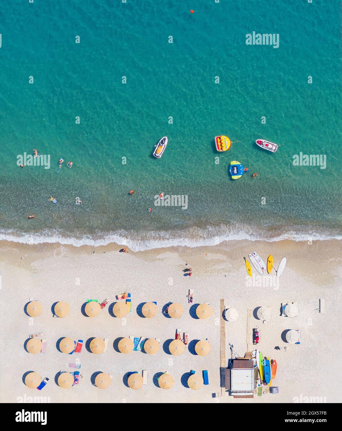 Vista aerea della spiaggia di sabbia direttamente sopra, scatto verticale. Lettini, ombrelloni e attrezzature per sport acquatici, persone che nuotano e prendono il sole Foto Stock