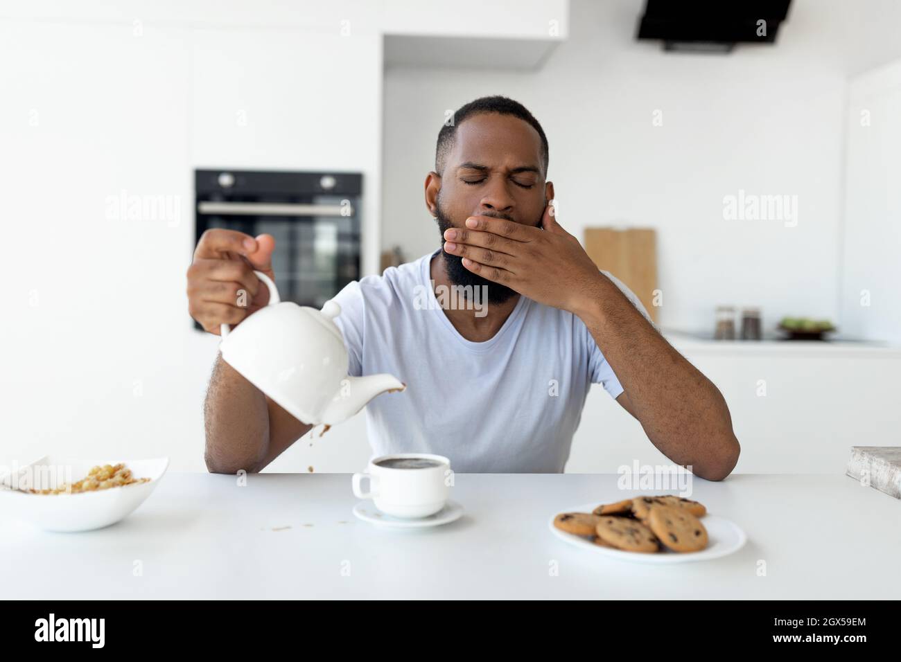 Il ragazzo nero che versa il caffè via dalla tazza e dal yawning Foto Stock