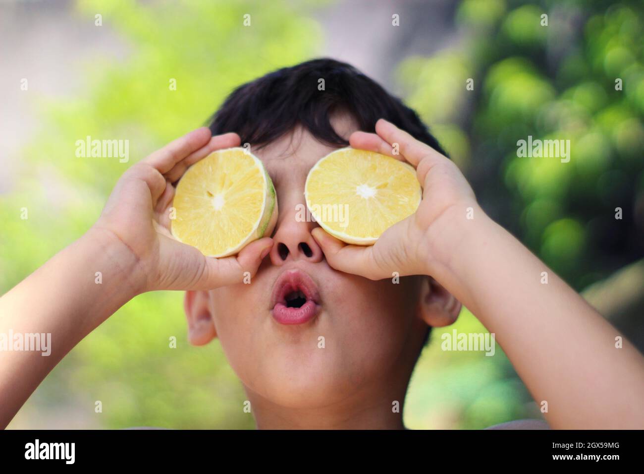 Giocoso ragazzo ispanico cubano che tiene due metà di un limone davanti agli occhi Foto Stock