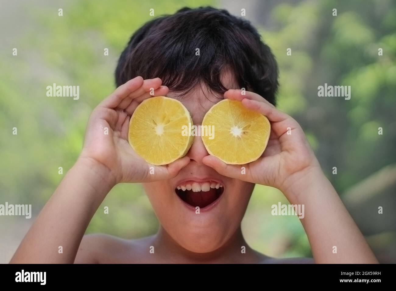 Giocoso ragazzo ispanico cubano che tiene due metà di un limone davanti agli occhi Foto Stock