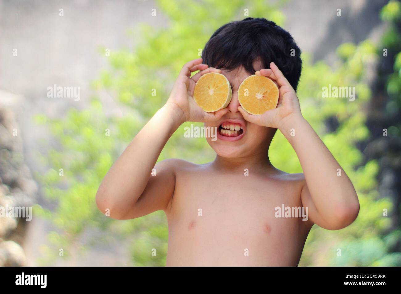 Giocoso ragazzo ispanico cubano che tiene due metà di un limone davanti agli occhi Foto Stock