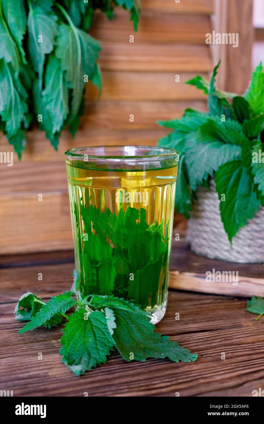 Tisane curative con ortica. Tè in un bicchiere su un tavolo di legno. Rimedio popolare. La fonte di vitamine e antiossidanti. Foto Stock