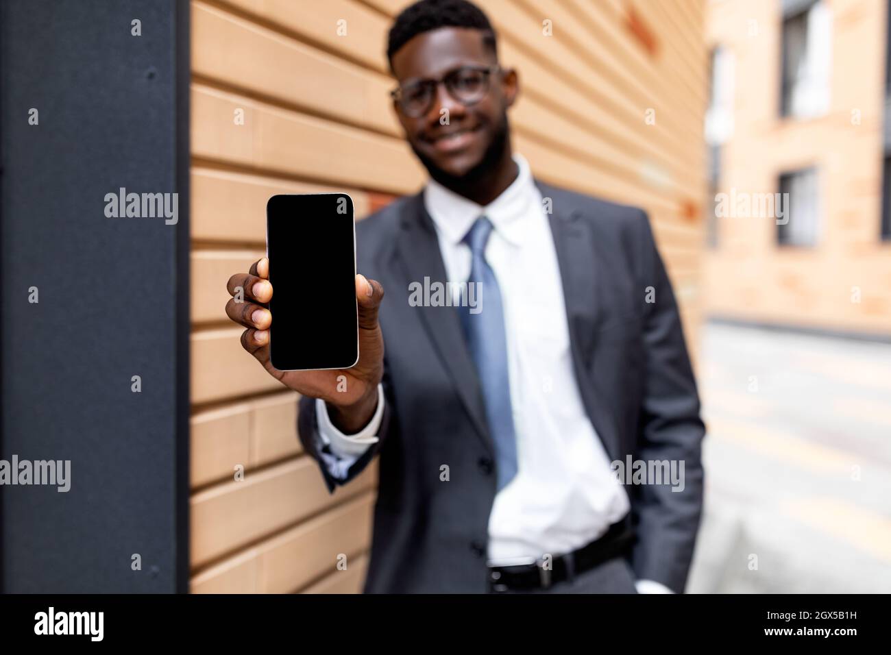 Tecnologie moderne e business concept. Uomo d'affari felice nero che mostra smartphone con schermo vuoto Foto Stock