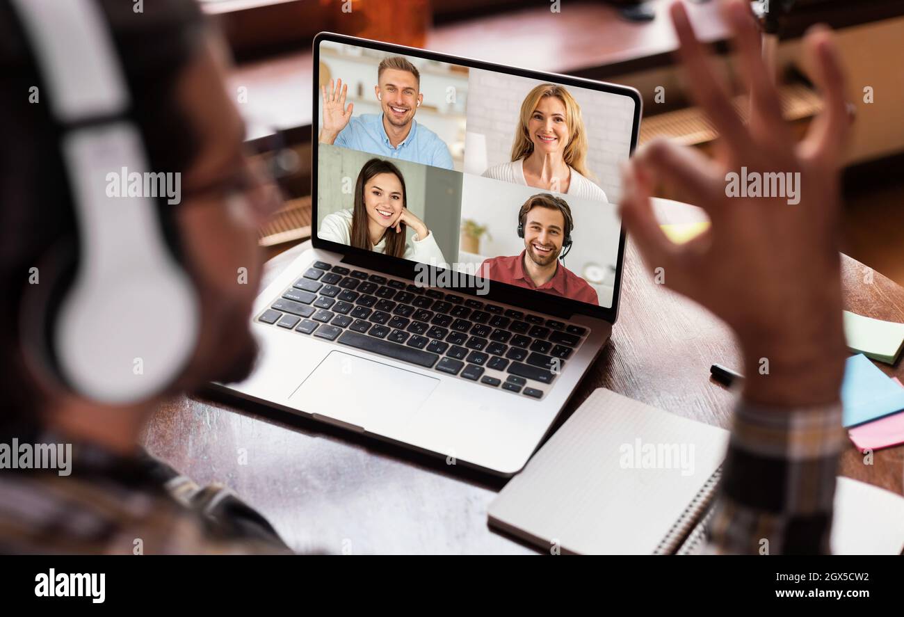 Crosed giovane indiano ragazzo hanno videochiamata con headshot di diverse persone europee sullo schermo del computer e mostrare ok segno Foto Stock