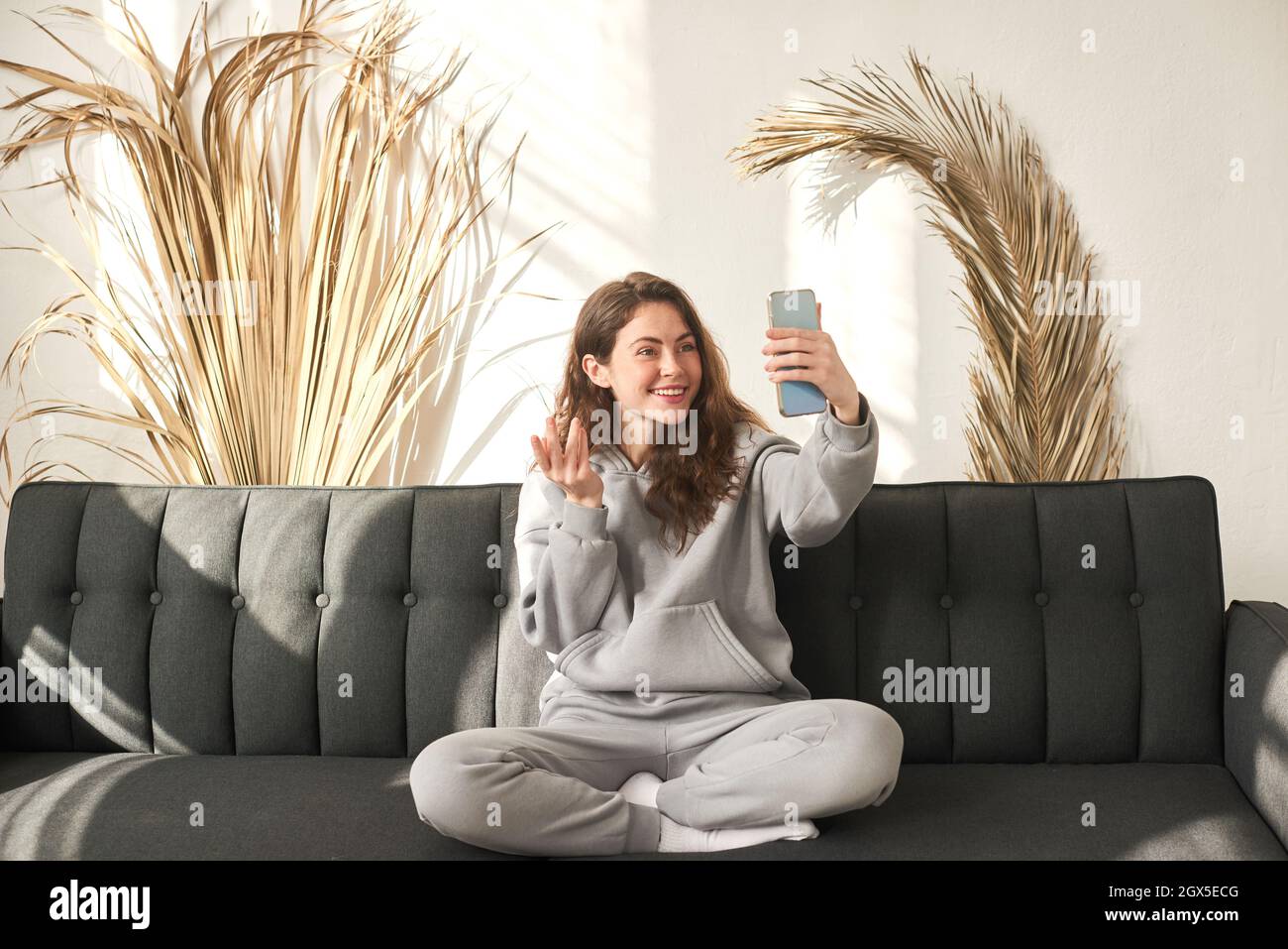 Una donna felice che effettua videochiamate in tempo reale con lo smartphone a casa, utilizzando l'app online per riunioni con zoom, social distancing, lavora da casa Foto Stock