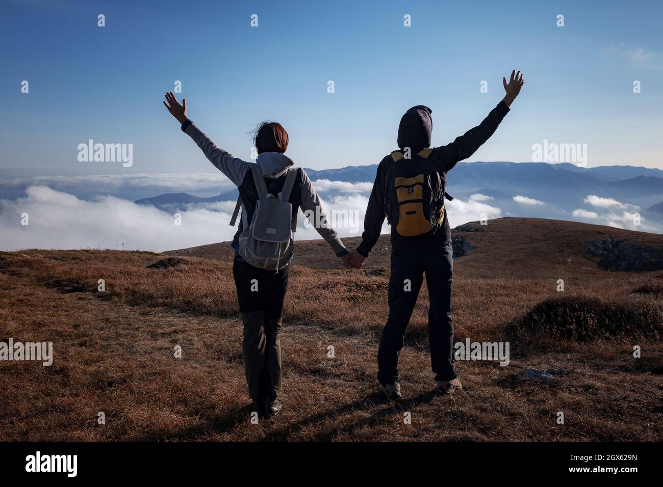 Escursioni avventura sano all'aperto persone in piedi parlare. Coppia godendo vista sopra le nuvole sul trekking. Giovane donna e uomo in natura indossando zaini e bastoni da trekking. Foto Stock