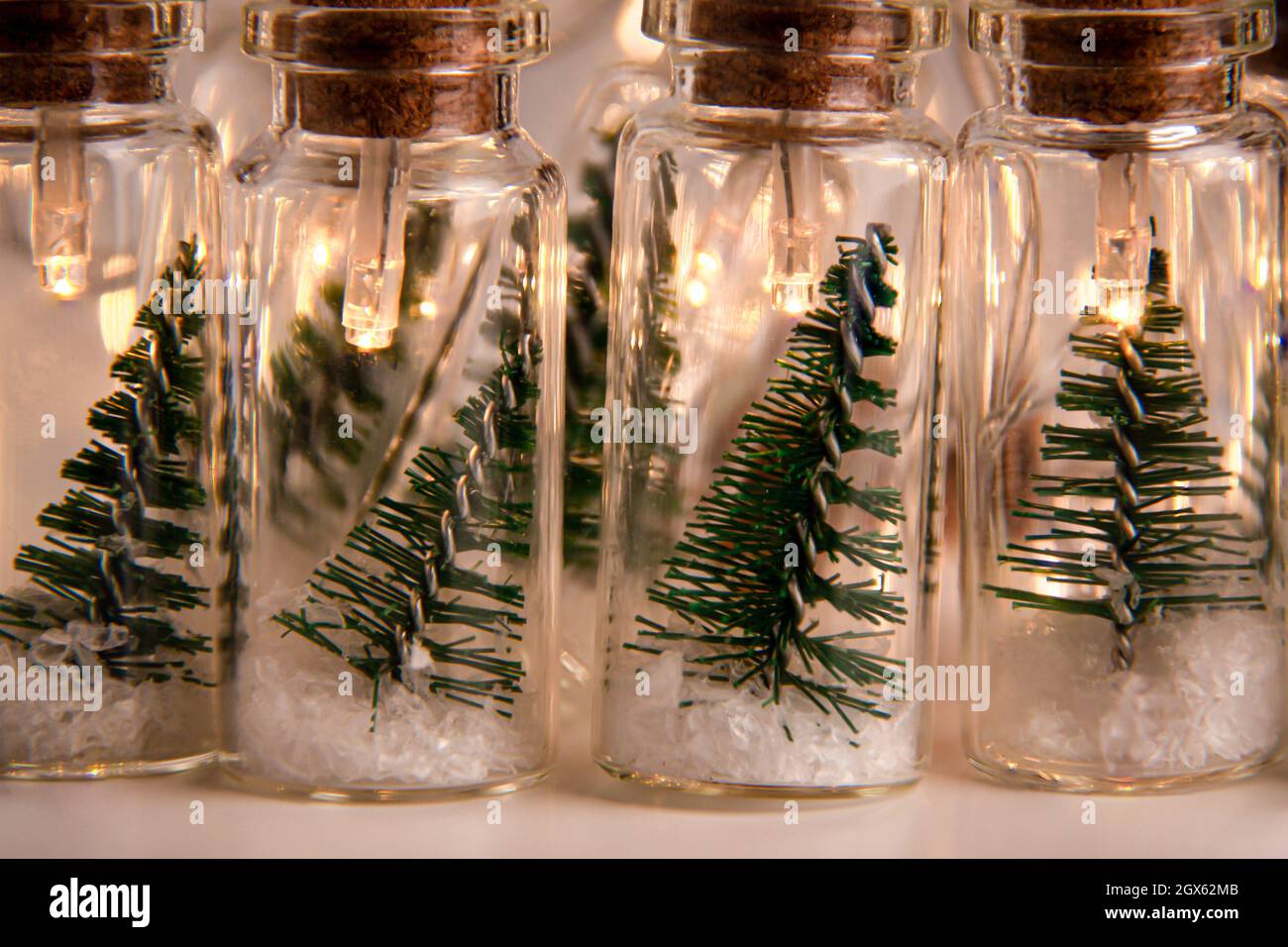 Primo piano di luci incandescenti decorazione di vasi di vetro con tappi  all'interno dei quali ci sono piccoli alberi verdi di Natale su neve  artificiale. Vacanze nuovo Yea Foto stock - Alamy