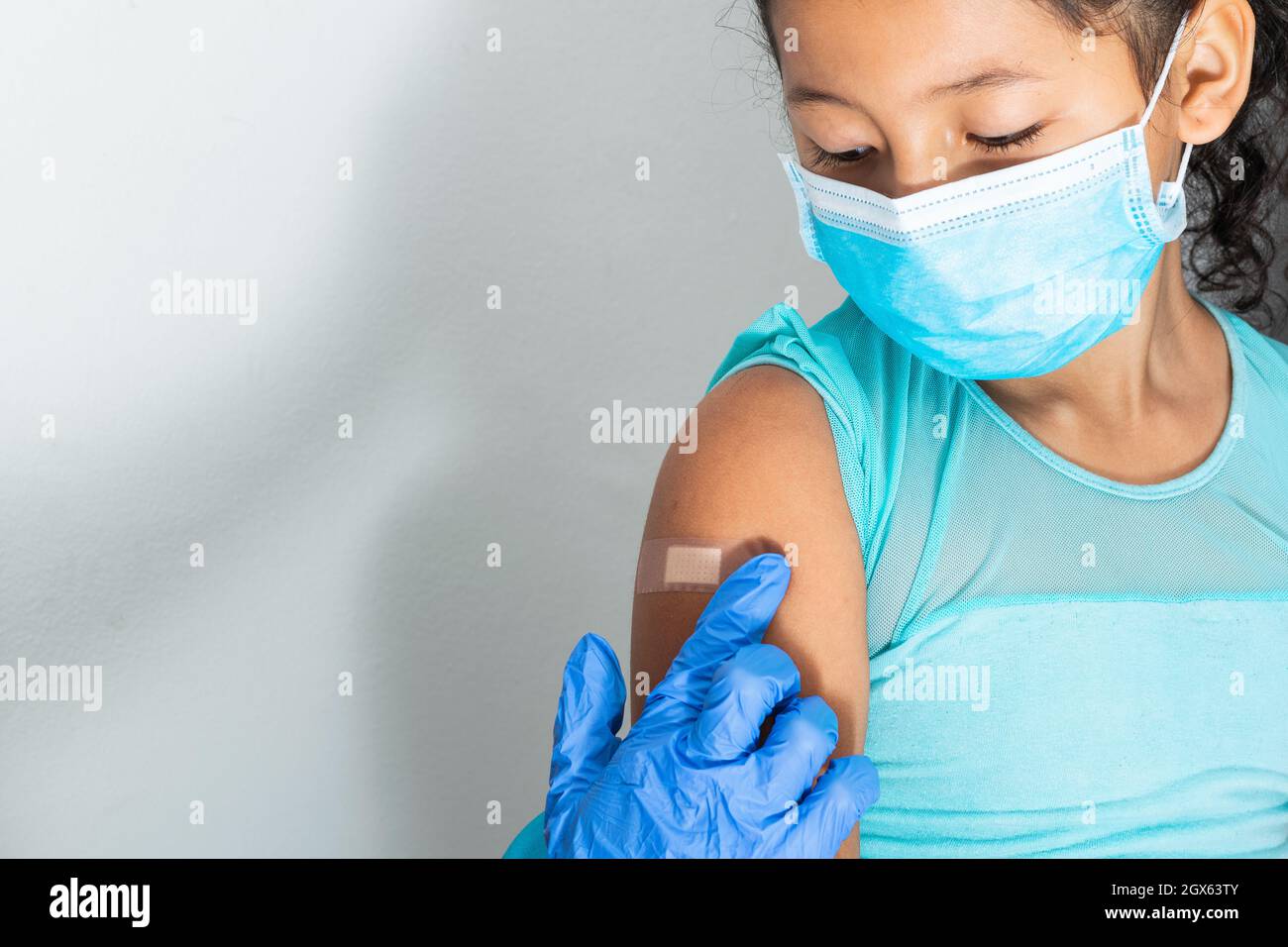 Medico in guanti protettivi di gomma blu mettendo un bendaggio adesivo sul braccio di una ragazza dopo aver ferito la pelle o iniettato il vaccino. Pronto soccorso. Medico, p Foto Stock