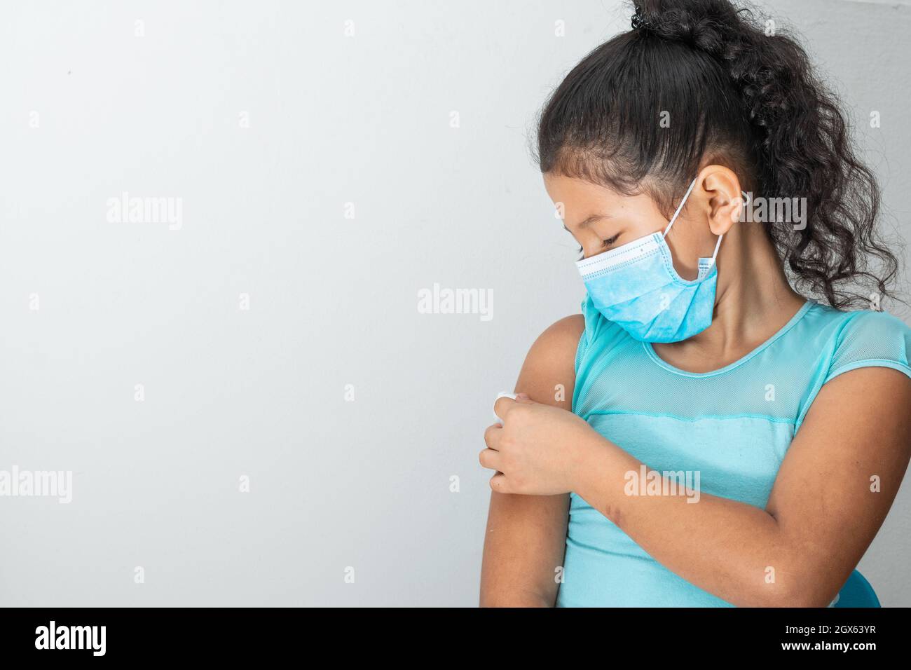 bambina che tiene un batuffolo di cotone sul braccio dopo aver ferito la pelle o aver iniettato il vaccino covid-19. Pronto soccorso. Medico, farmaceutico e sanitario Foto Stock