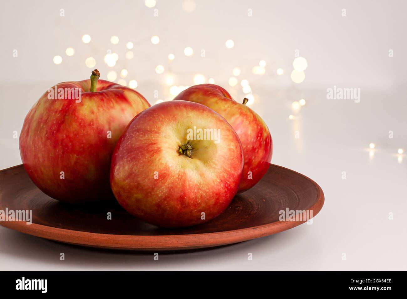Primo piano delle mele rosse gialle con gocce d'acqua sul piatto marrone scuro su sfondo luminoso con bokeh giallo oro. Alimenti biologici sani, umore autunnale Foto Stock
