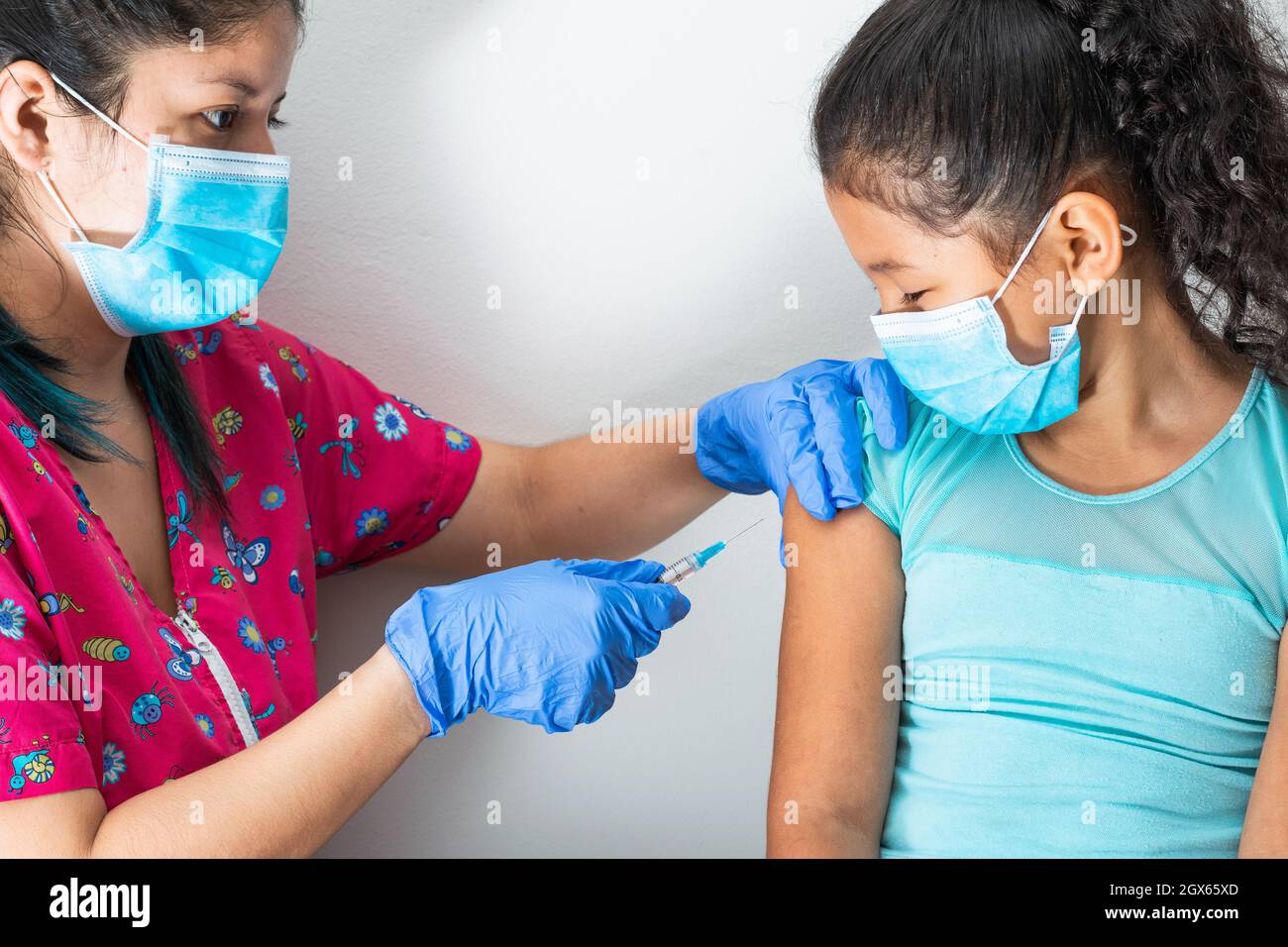 l'infermiera dei bambini inietta il braccio della bambina marrone, mentre guarda il suo viso. le mani del medico con guanti di gomma che inietta il vaccino di covid-19 o di influenza. m Foto Stock