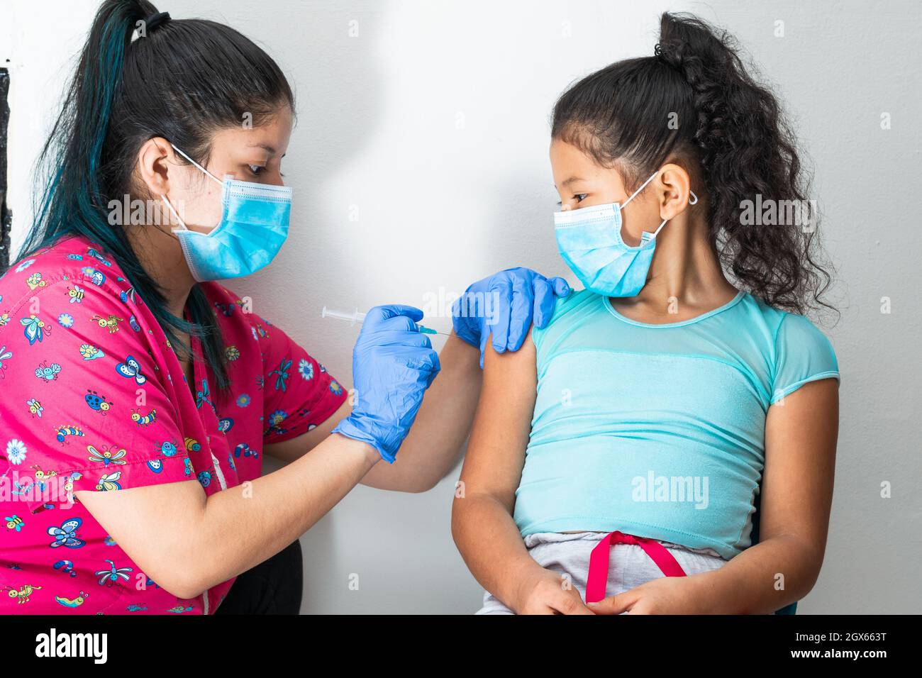 l'infermiere dei bambini inietta il braccio della bambina marrone. le mani del medico con i guanti di gomma che iniettano il covid-19 o il vaccino di flu. la ragazza seduta mentre è vac Foto Stock