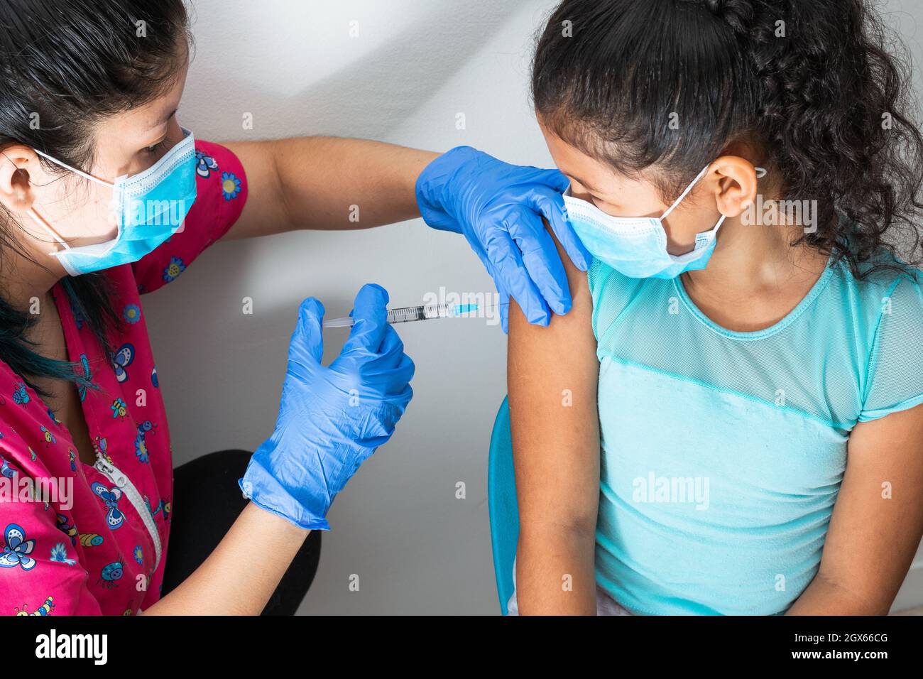 l'infermiere dei bambini inietta il braccio della bambina marrone. ragazza che guarda l'infermiere, le mani del medico con i guanti di gomma che inietta il vaccino di covid-19. il vaccino di flu. m Foto Stock