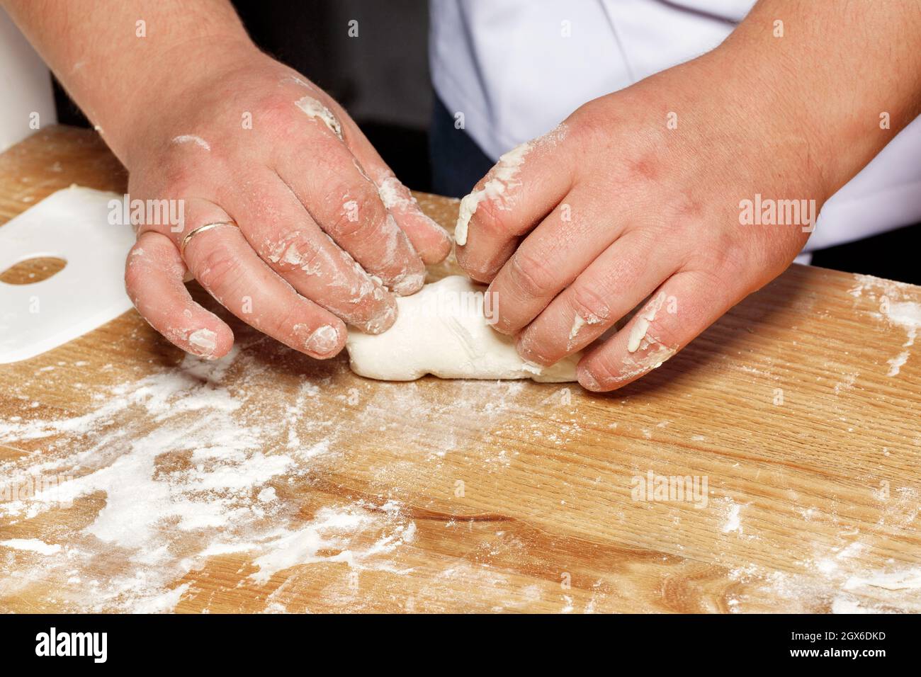 Mani maschili di un uomo caucasico che prepara pasta per pizza su un tavolo da cucina in legno. Primo piano, spazio di copia. Foto Stock