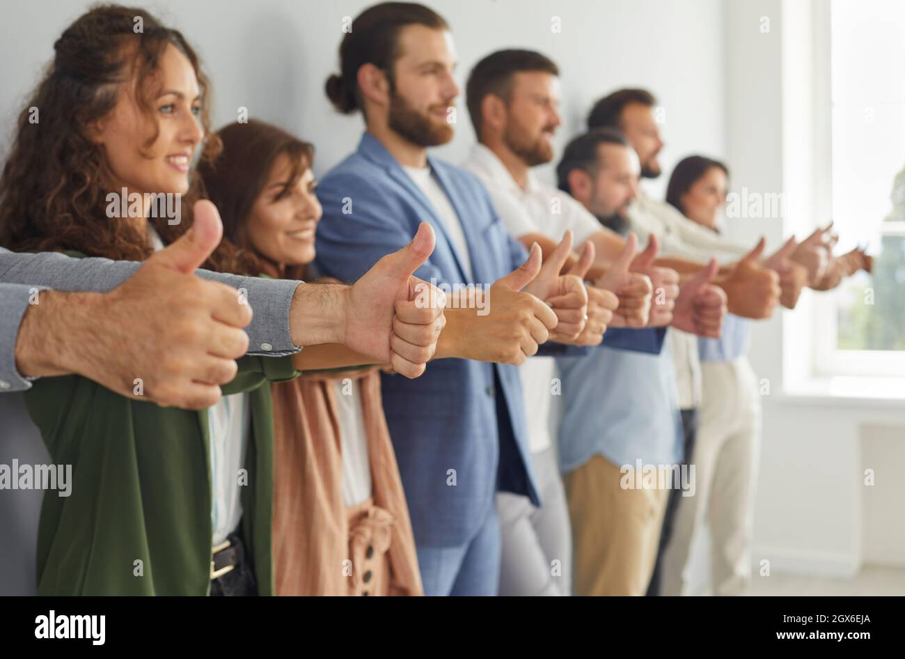 Squadra di gente felice di affari che si levano in piedi in fila e che mostra i thumbs in su il gesto tutti insieme Foto Stock