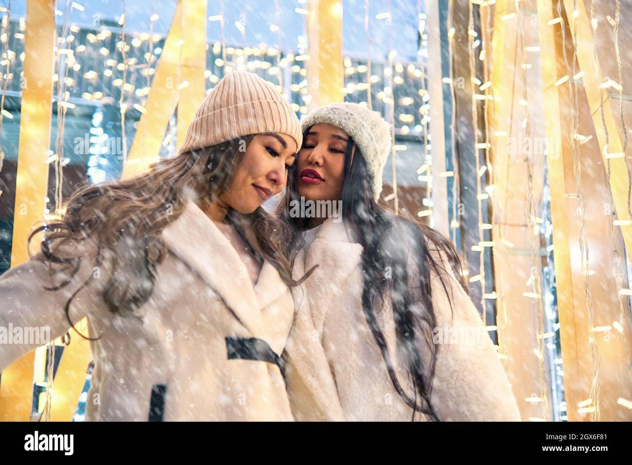 Due ragazze asiatiche in cappotti bianchi stanno avendo divertimento abbracciare, anno nuovo, lampadine Foto Stock