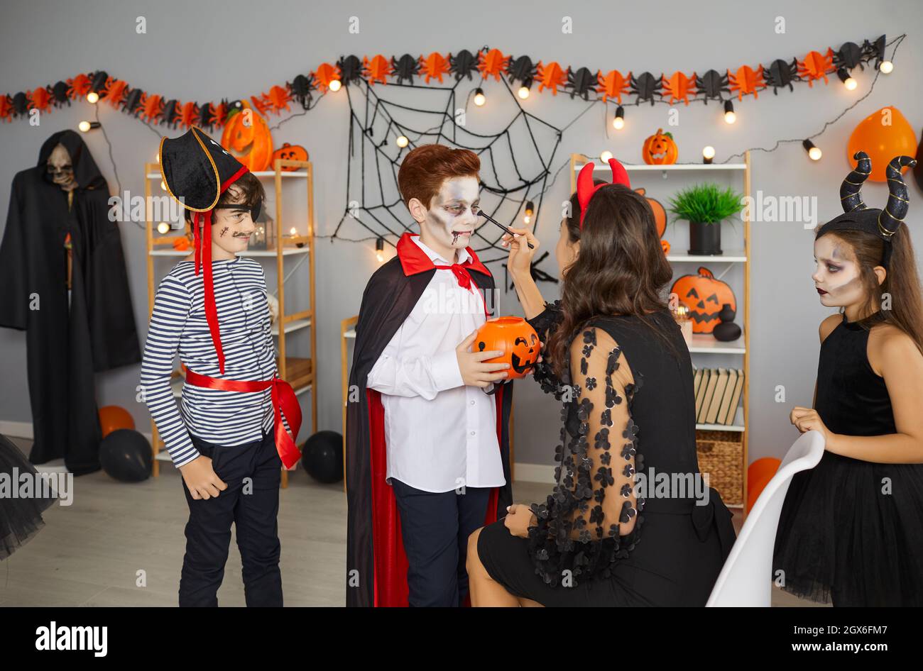 La donna rende i bambini trucco spooky preparandoli per il partito tradizionale di Halloween. Foto Stock
