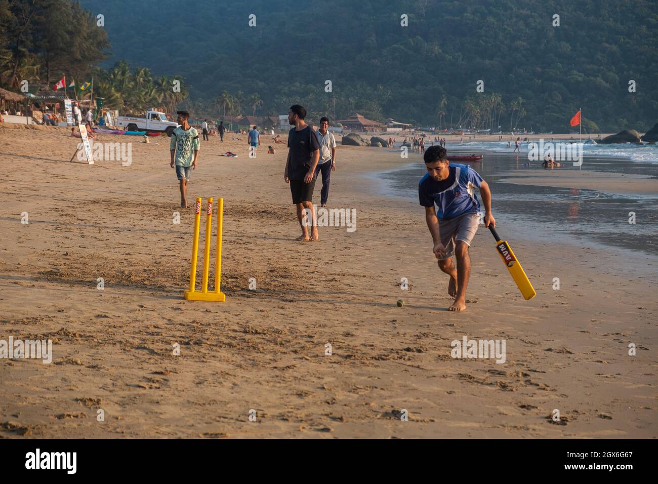 Gruppo di adulti indiani che giocano a cricket sulla spiaggia al tramonto, Goa, India Foto Stock