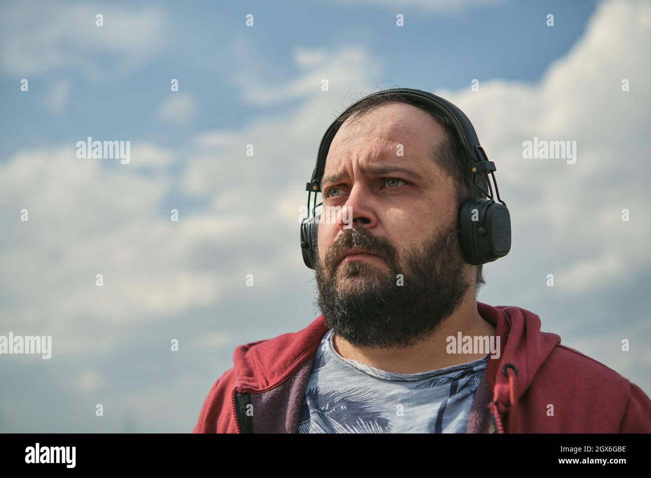 Uomo europeo di mezza età in cuffia all'aperto che ascolta la musica sullo sfondo del cielo Foto Stock