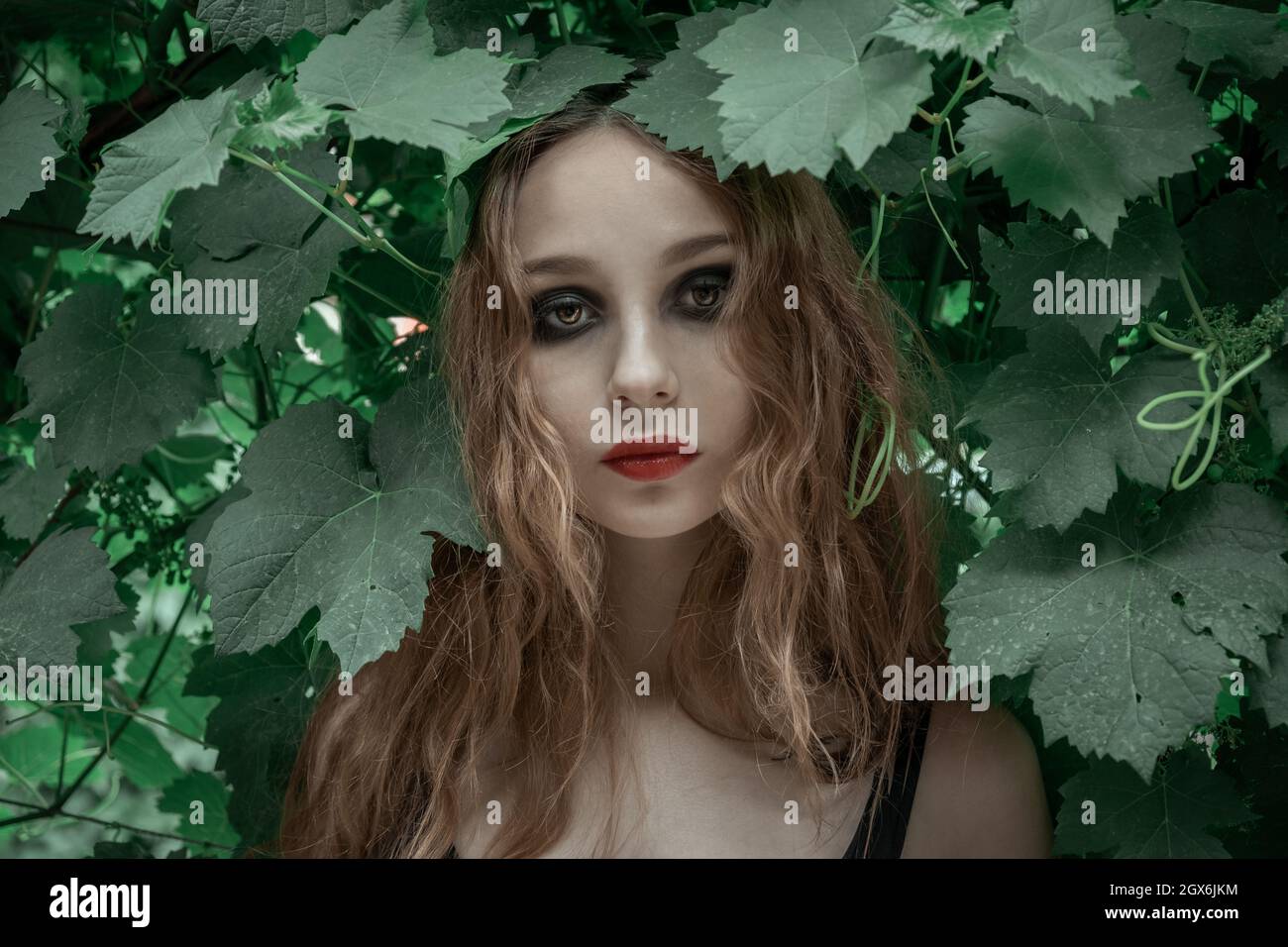 Ritratto di bella giovane donna con labbra rosse che rimangono davanti alle foglie verdi Foto Stock