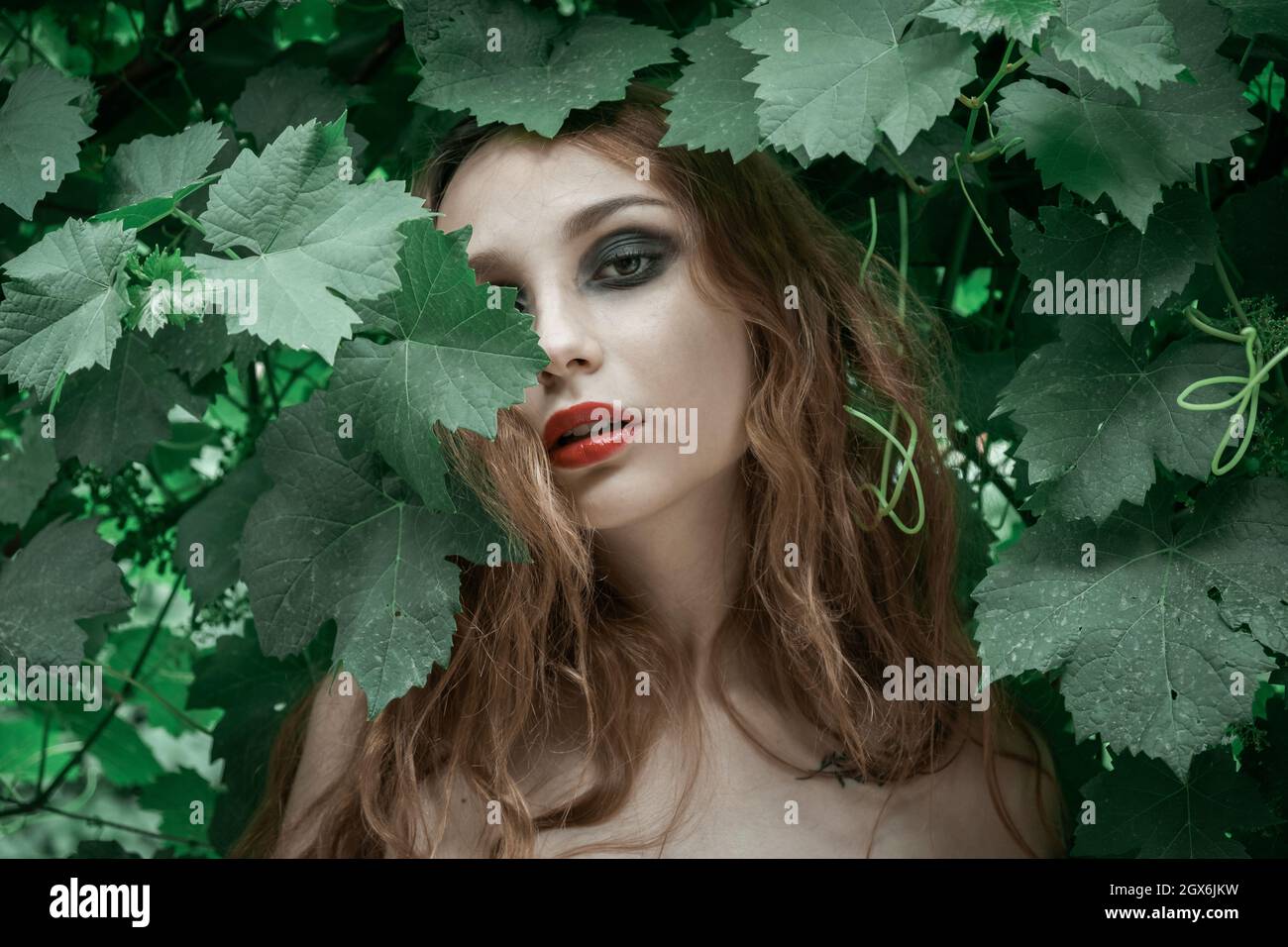 Ritratto di bella giovane donna con labbra rosse che rimangono davanti alle foglie verdi Foto Stock