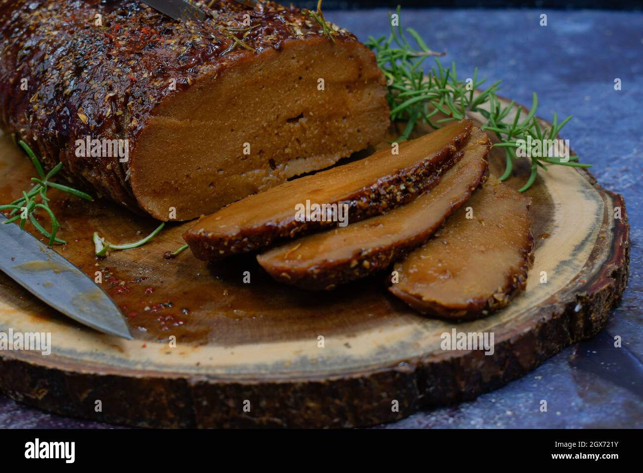Seitan arrosto strofinato con spezie e salsa barbecue su tavola di legno, affettato, spazio copia Foto Stock