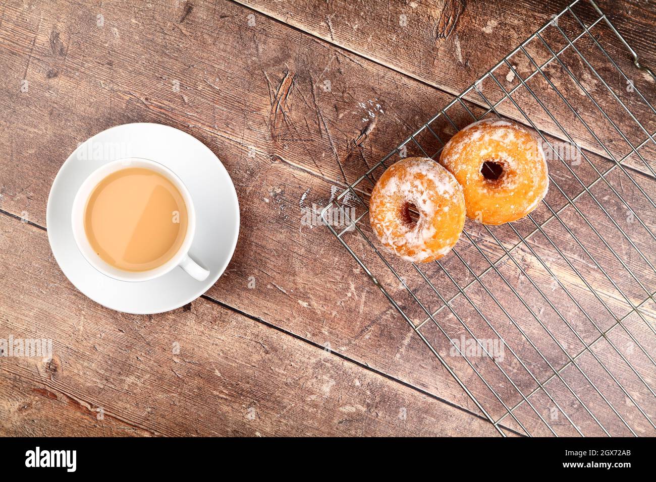 Tavolo in legno con una tazza di tè e ciambelle appena sfornate adagiato su una griglia di raffreddamento a filo Foto Stock