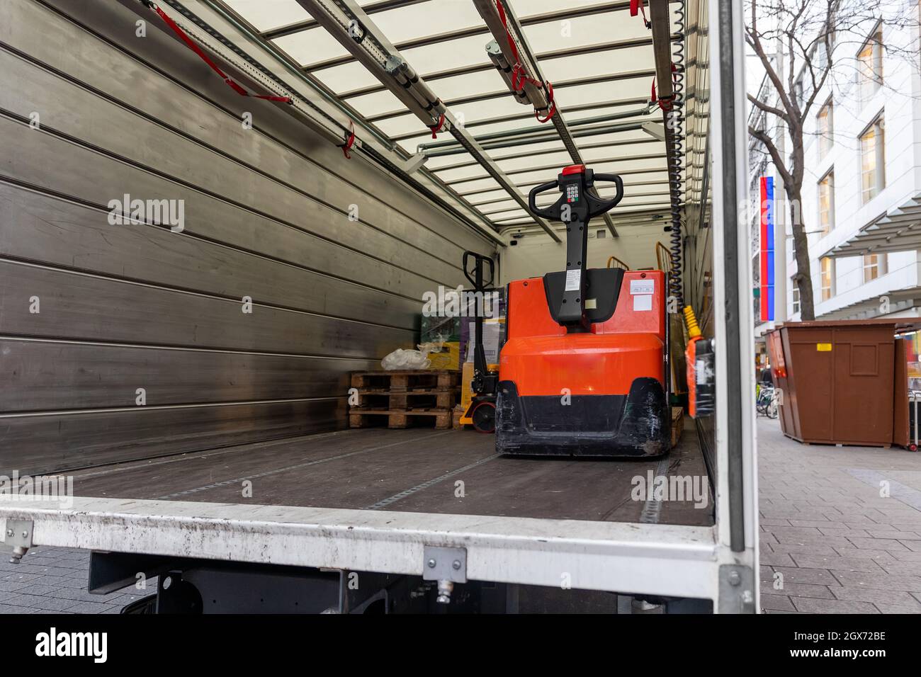 Piccolo cargo bianco di medie dimensioni parcheggiato per lo scarico del portellone aperto con piccolo carrello elevatore a forche sulla strada urbana europea. Consegna rapida tramite corriere espresso Foto Stock