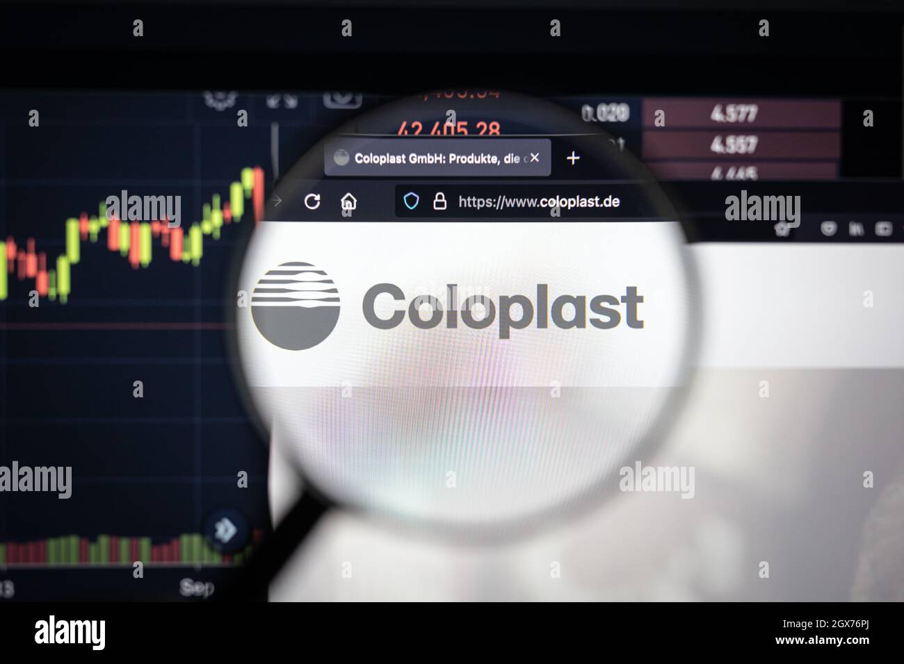 Il logo dell'azienda di Coloplast su un Web site con gli sviluppi blurry del mercato azionario nello sfondo, visto su uno schermo del calcolatore attraverso una lente d'ingrandimento Foto Stock