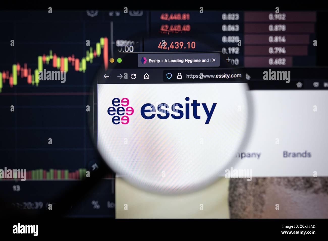 Essity Company logo su un sito web con blurry di mercato azionario sviluppi in background, visto su uno schermo di computer attraverso una lente d'ingrandimento Foto Stock