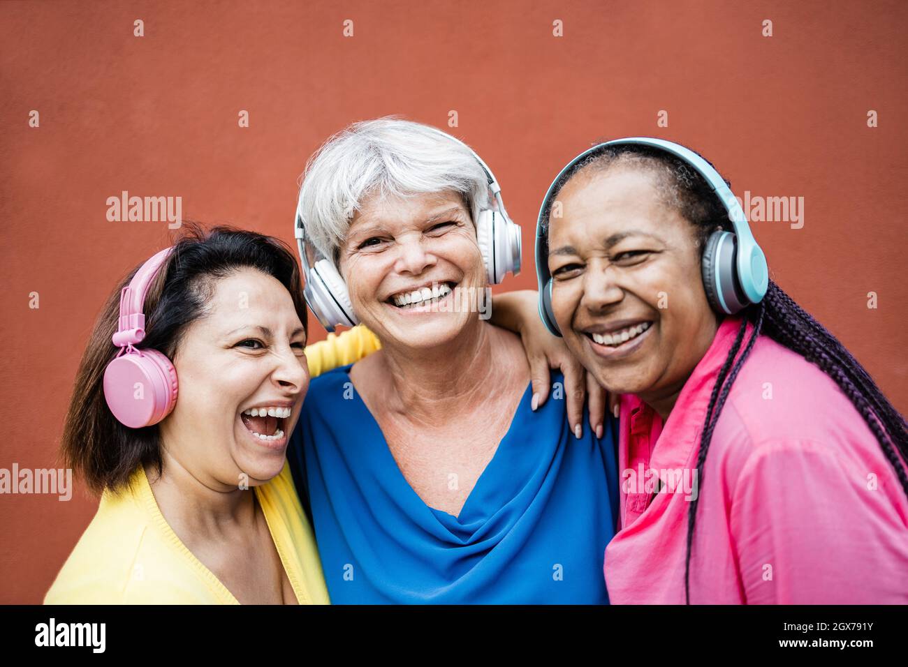 Donna anziana multirazziale divertirsi ascoltando musica playlist con le cuffie insieme - concetto di stile di vita anziano - Focus sul volto centrale donna Foto Stock
