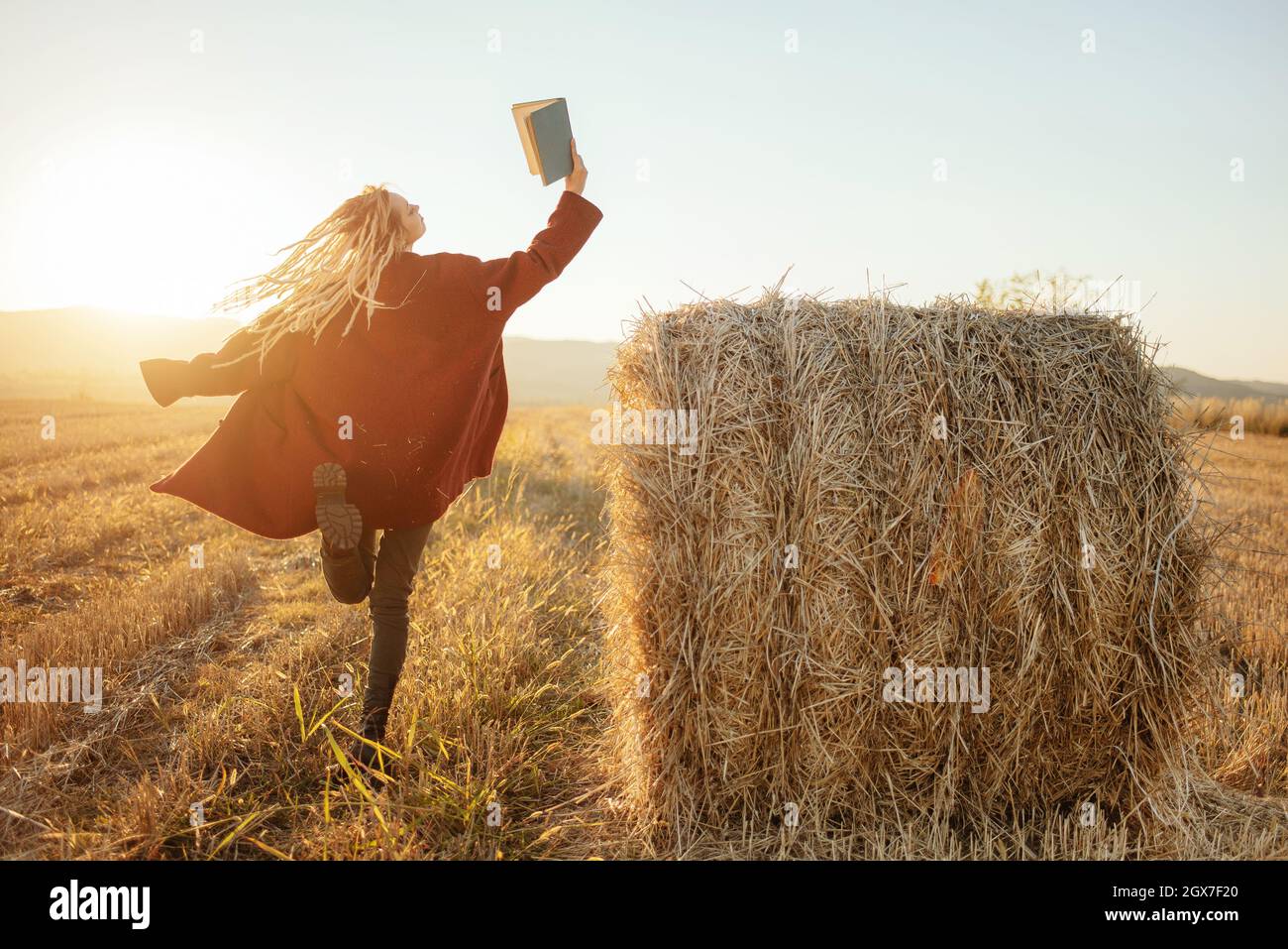 Ragazza allegra, ballando e saltando mentre legge un libro emozionante nel campo fuori Foto Stock