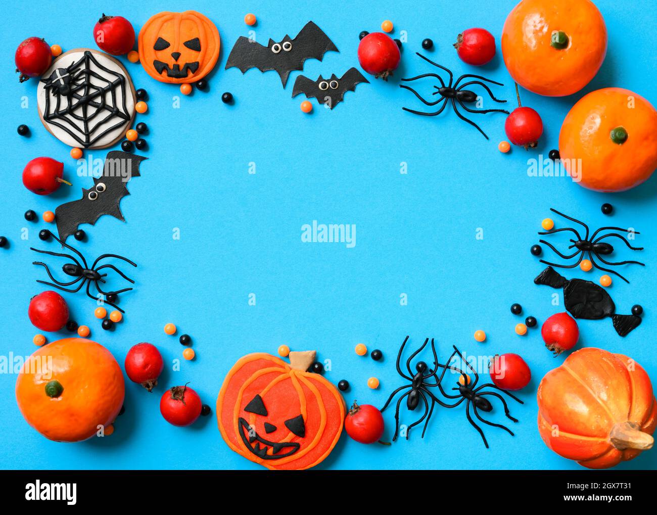 Sfondo di Halloween con ragni e pipistrelli, piatto. Cornice con personaggi divertenti di Halloween sul tavolo blu, vista dall'alto. Hallowen cibo e decorazioni per gr Foto Stock