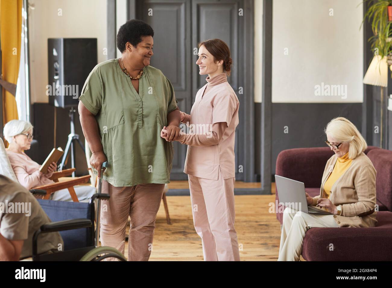 Ritratto di giovane donna sorridente che aiuta gli anziani nella casa di pensione moderna, spazio copia Foto Stock