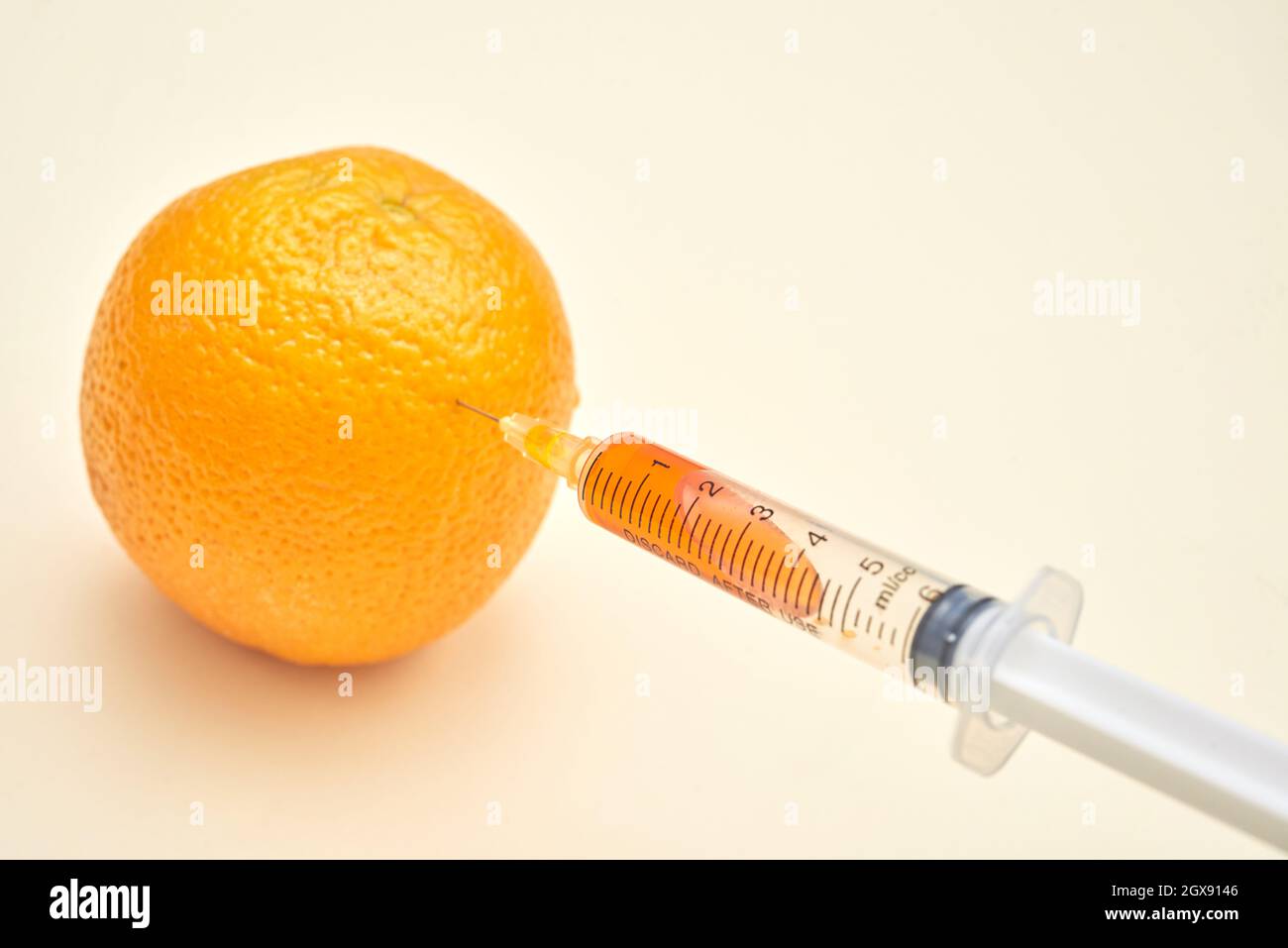 Primo piano della siringa per l'iniezione di arancione con liquido arancione, gmo Concept Foto Stock