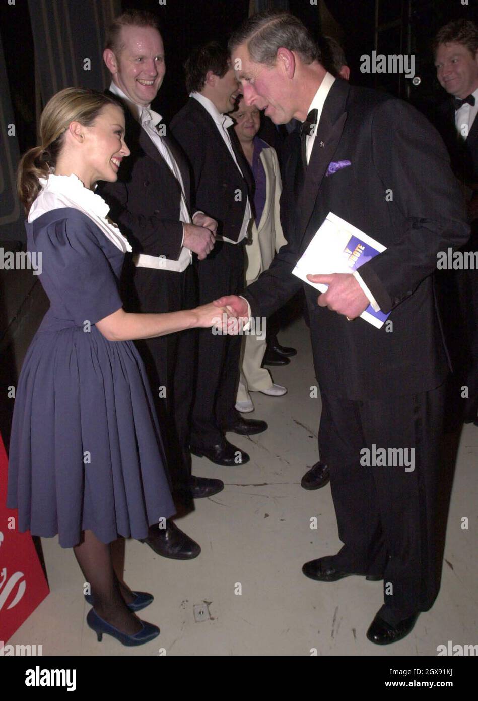 Il Principe di Galles incontra Kylie Minogue, ospite a sorpresa al Wyndham Theatre di Londra per una performance Royal Gala "Princes Trust" di "The Play What i wrote" diretta da Kenneth Branagh. A tutta lunghezza, abito blu, frill bianco, cantante, moda, shake a mano. Foto Stock