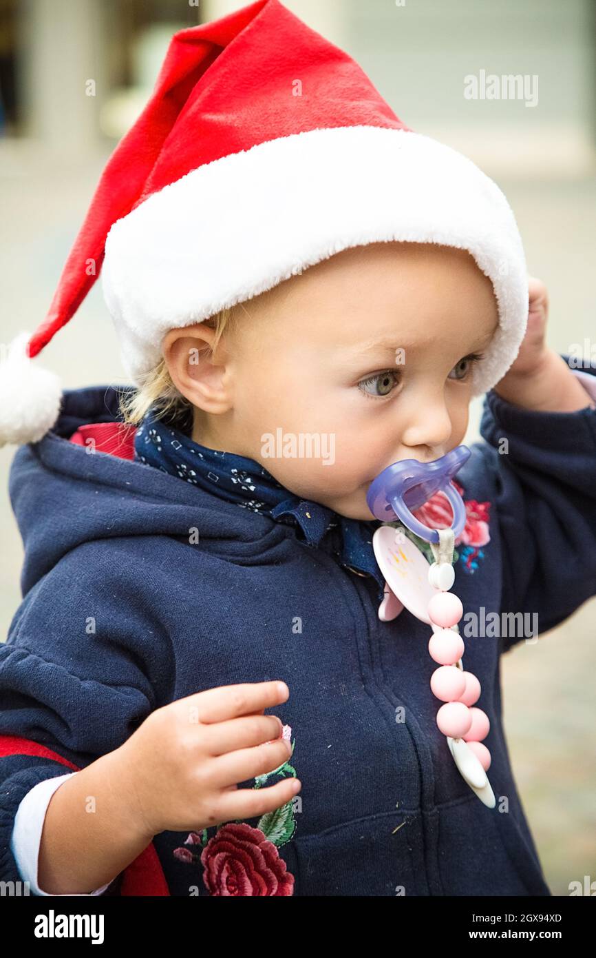 Profilo ragazza del bambino dell'occhio blu. Cappello rosso di Natale, cappotto blu e ciuccio succhietto. Corsa di nuovo anno. Sbrigati per Natale. Concetto di sconti per acquisti invernali Foto Stock