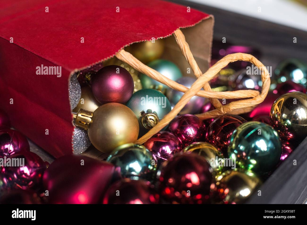 Borsa regalo di carta rossa piena di colorati giocattoli di Natale. Preparazione dei regali. Decorazioni multicolore per il nuovo anno per piccolo albero di Natale. Foto cartolina Foto Stock