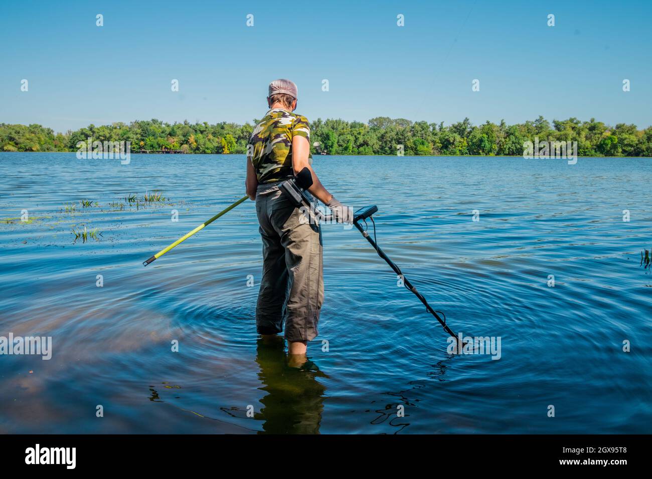 Una donna cerca metalli preziosi nel fiume con un metal detector. Foto Stock