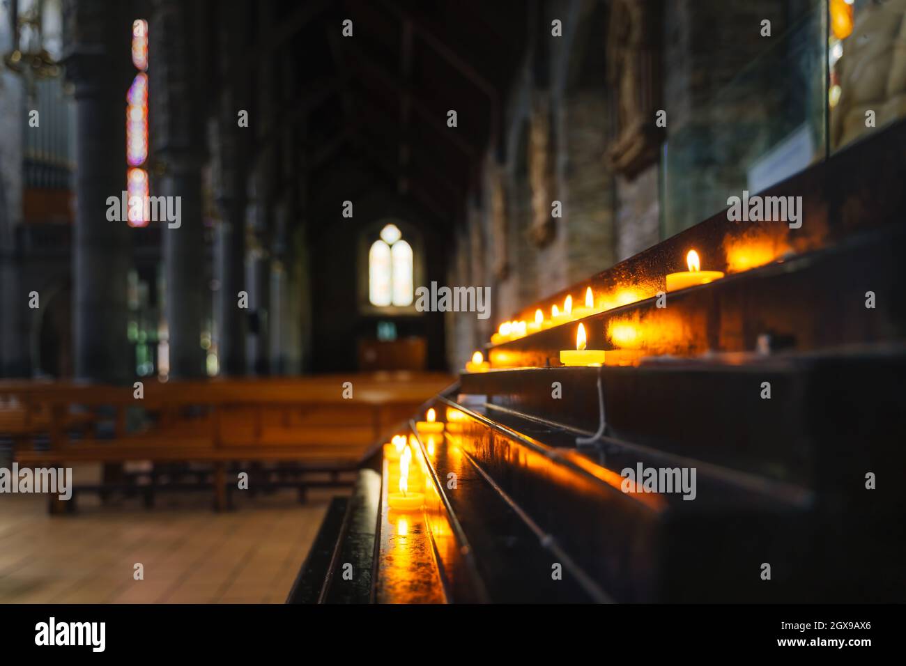 Fuoco selettivo su candela votiva illuminata con luce soffusa e luminoso e sfondo sfocato dell'interno della Cattedrale di St. Marys a Killarney, Kerry, Irlanda Foto Stock