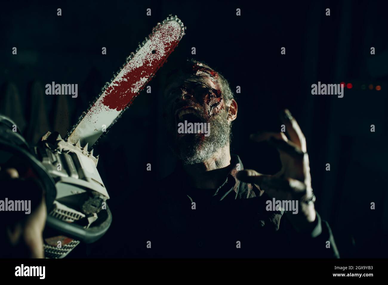 Spaventoso zombie e chainsaw difesa Halloween concetto partito. Preparare la pelle e il sangue sul viso Foto Stock