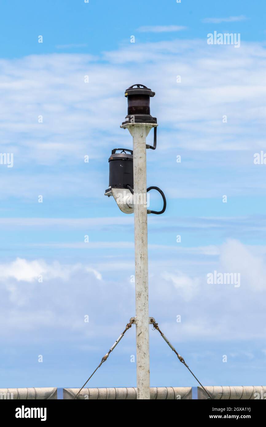 Palo di poppa della nave con due luci di navigazione contro il cielo blu nuvoloso. I tenditori e i fili di acciaio tengono l'asta in posizione verticale. Foto Stock