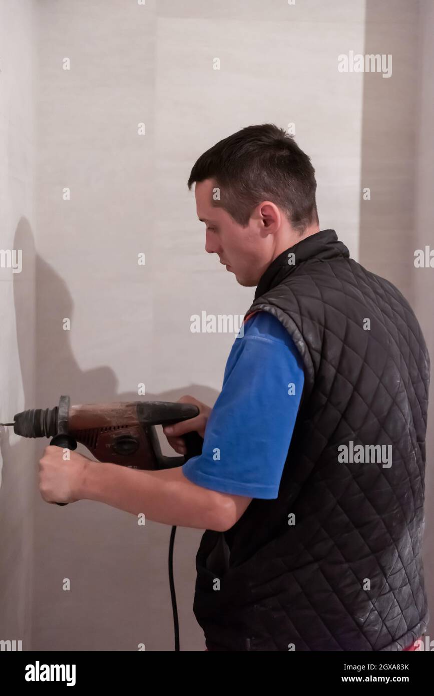 giovane professionista di costruzione che perfora i fori nella parete della stanza da bagno per installare gli accessori della stanza da bagno Foto Stock