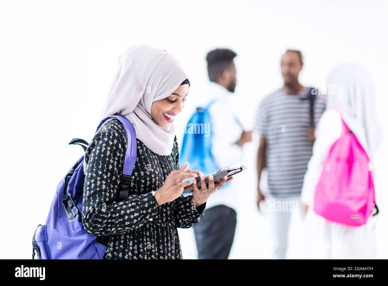 Giovani Musulmani moderni femmina africana studente utilizzando computer tablet con un gruppo di amici in background indossando il tradizionale hijab islamico vestiti Foto Stock